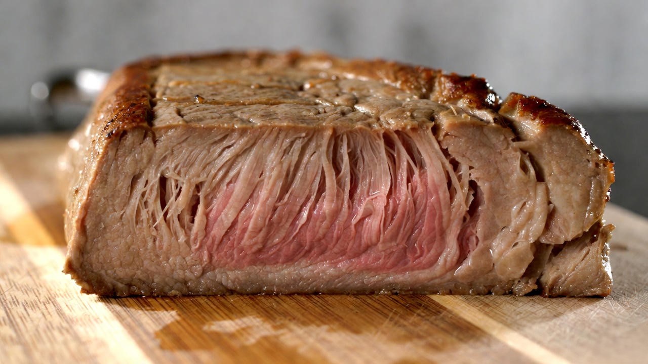 Close-up sliced vegan seitan steak showing realistic fibrous texture and juicy pink interior, perfect plant-based George Martin strip steak alternative