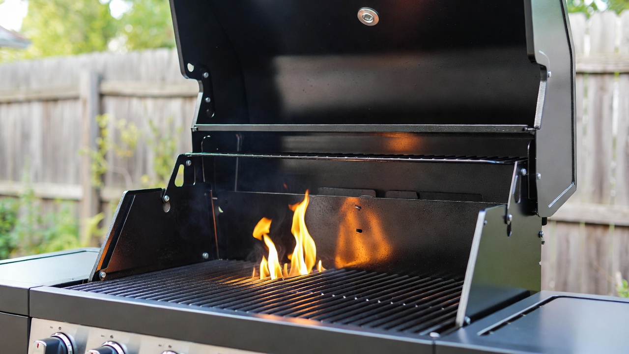 Close-up of Dyna-Glo grill interior showing burners, heat plates, grates, and grease tray for easy part identification