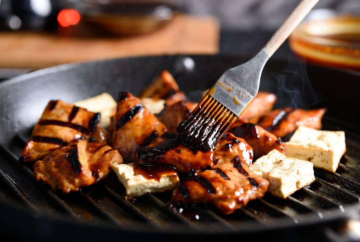 Plant-based grilled teriyaki chicken being basted with homemade glossy sauce on a grill pan